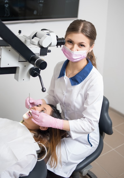 Femme dentiste avec des outils dentaires - microscope, miroir et sonde vérifiant les dents des patients au bureau de la clinique dentaire