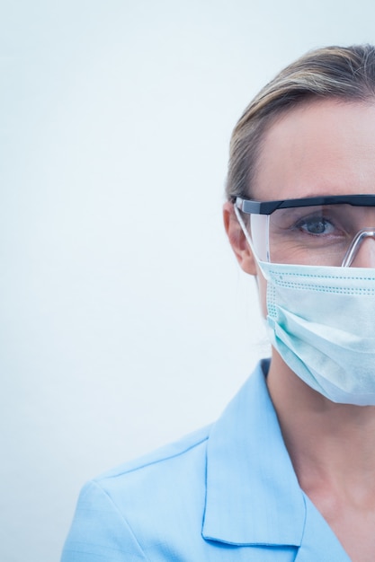 Femme dentiste portant un masque chirurgical et des lunettes de sécurité