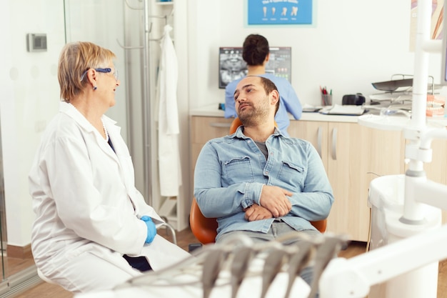 Femme dentiste senior discutant avec le patient du traitement des maux de dents lors d'une consultation stomatologique au bureau de l'hôpital dentaire