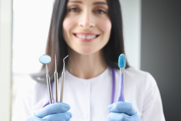 Femme dentiste souriante tenant un outil et une brosse à dents dans ses mains