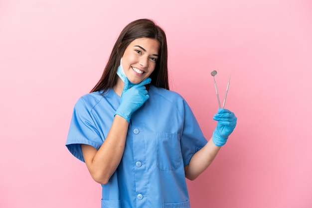 Femme dentiste tenant des outils isolés sur fond rose heureux et souriant