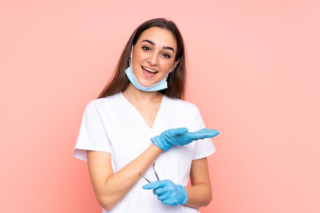 Femme dentiste tenant des outils isolés sur un mur rose étendant les mains sur le côté pour inviter à venir