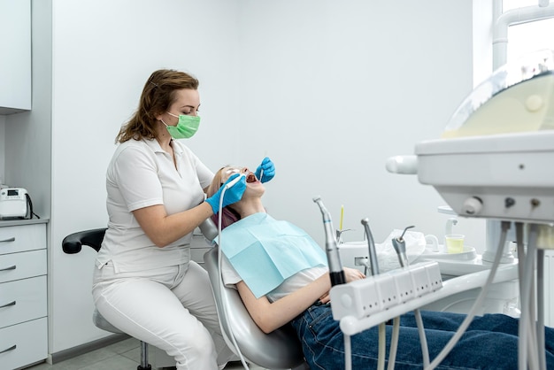 Femme dentiste traite les dents d'une jeune fille patiente allongée dans la clinique de dentisterie dents saines de la cavité buccale sourire