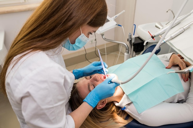 Une femme dentiste traite les dents d'un patient Le dentiste effectue un nettoyage professionnel des dents d'une jeune patiente au cabinet dentaire