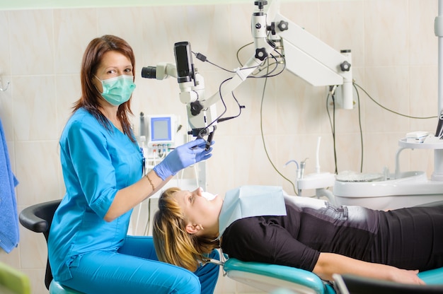 Femme dentiste travaillant au microscope au bureau de stomatologie moderne