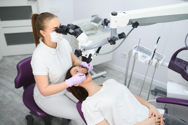 Femme dentiste utilisant un microscope dentaire traitant les dents du patient au bureau de la clinique dentaire