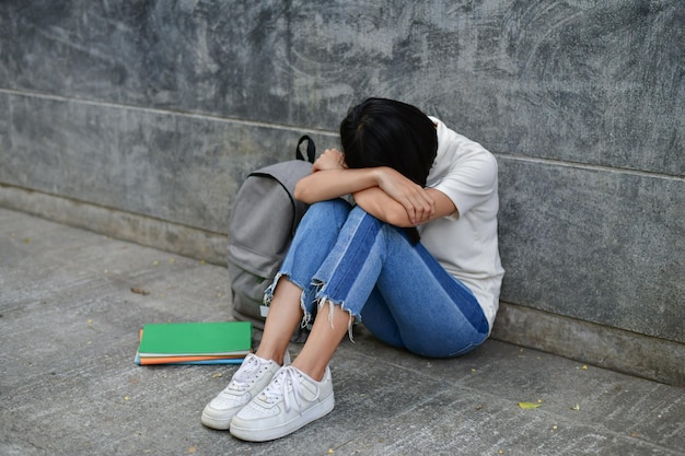 Une femme déprimée assise sur un trottoir contre un mur gris.