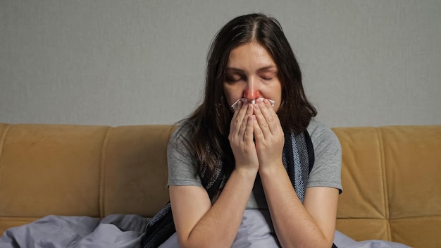 Une femme déprimée avec le nez qui coule est assise sur un canapé dans le salon