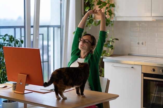 Femme dérangée par un chat debout sur une table au bureau à domicile L'animal veut recevoir l'attention du propriétaire