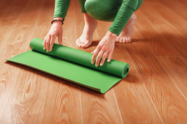 Une femme déroule un tapis vert avant un cours de yoga.