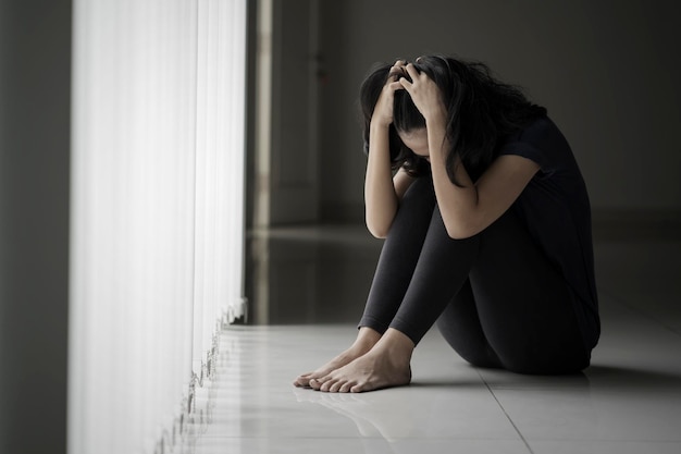 Une femme désespérée assise près de la fenêtre.