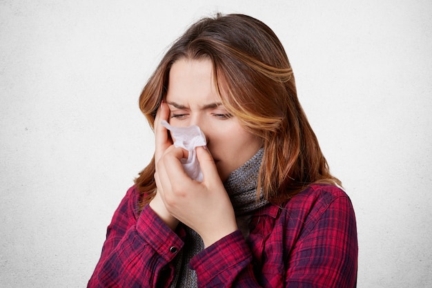 Une femme désespérée malade a la grippe, le nez qui coule, le nez dans un mouchoir, a de terribles maux de tête