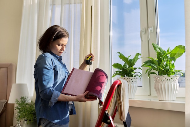 Femme designer choisissant des tissus de rideaux mesurant la fenêtre avec un ruban à mesurer