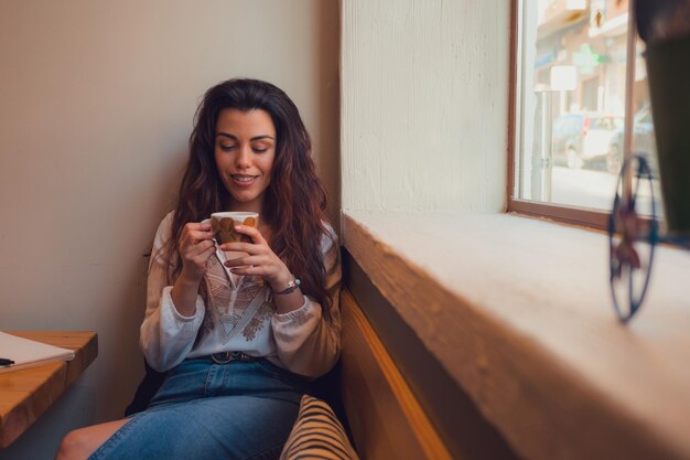 Une femme détendue buvant du café dans un restaurant alors qu'elle regarde par la fenêtre