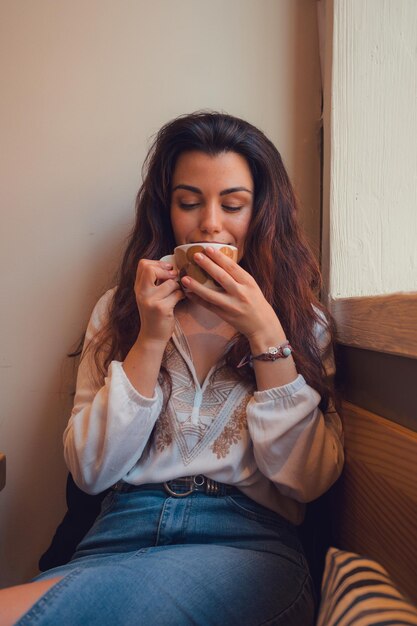 Une femme détendue buvant du café dans un restaurant alors qu'elle regarde par la fenêtre