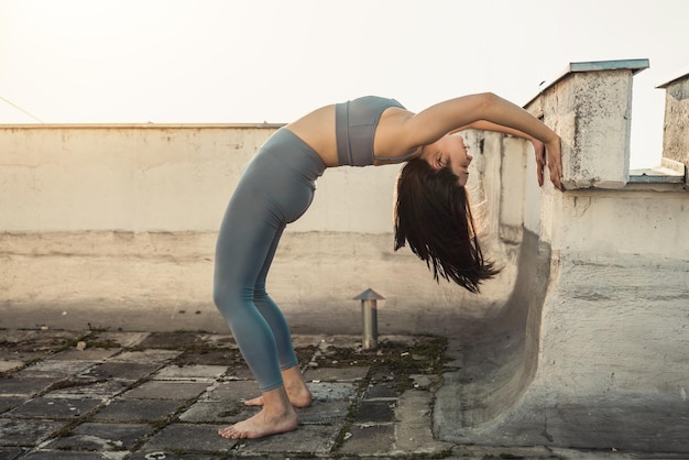 Femme détendue faisant de l'exercice d'étirement tout en pratiquant le pont de yoga pose près du mur sur un toit-terrasse.