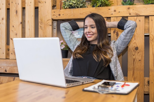 Femme détendue avec les mains derrière la tête à table avec ordinateur portable