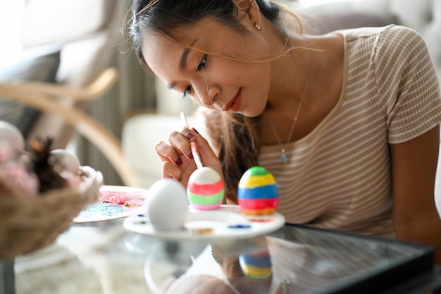 Femme détendue et palourde peignant sur un œuf de Pâques avec une couleur colorée dans son salon à la maison