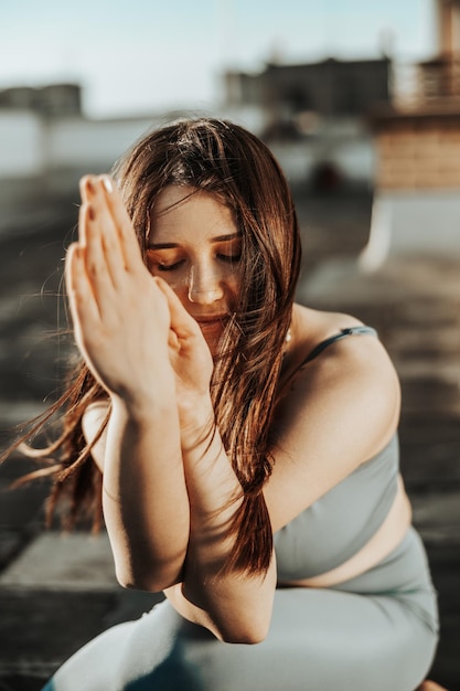 Femme détendue pratiquant le yoga sur un toit-terrasse au coucher du soleil.