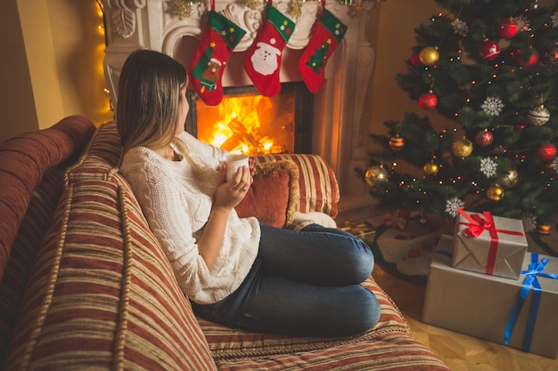 Femme détente au coin du feu et arbre de Noël avec une tasse de thé