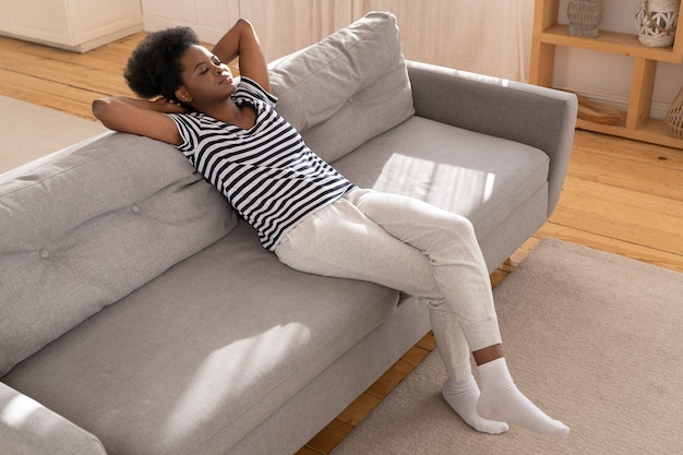 Femme de détente sur le canapé avec le bras sous la tête à la maison