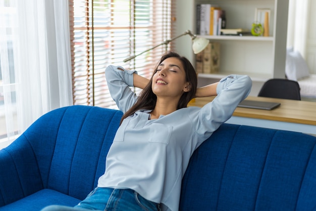 Photo femme détente sur canapé avec les yeux fermés et les mains derrière la tête à la maison