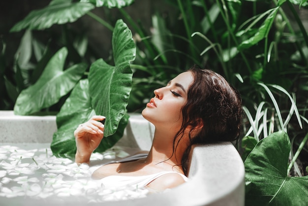 Femme détente dans un bain extérieur rond avec des fleurs tropicales.