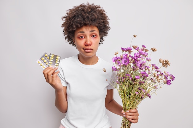 femme détient des médicaments sur l'allergie détient bouquet de fleurs sauvages se soucie de la santé a l'air malheureux malade isolated over white