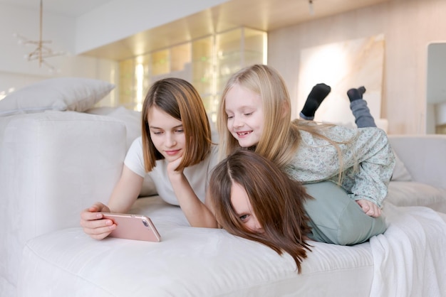 Une femme et deux enfants sont allongés sur un canapé. L'un d'eux regarde un téléphone.