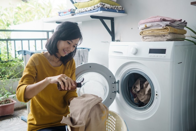 Femme devant la machine à laver faisant du linge de chargement de vêtements à l'intérieur