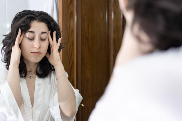 Une femme devant le miroir souffre de maux de tête.