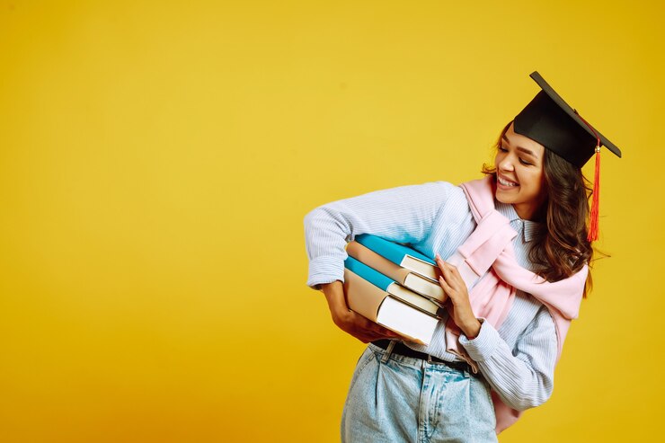 Photo femme diplômée dans un chapeau de graduation sur sa tête, avec des livres sur le jaune.