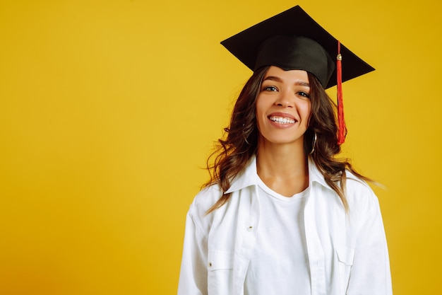 Femme diplômée dans un chapeau de graduation sur sa tête posant sur jaune