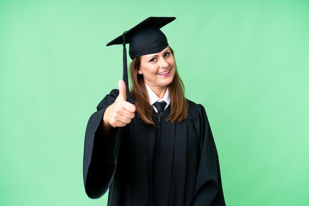 Femme diplômée de l'université d'âge moyen sur fond isolé avec les pouces vers le haut parce que quelque chose de bien s'est produit