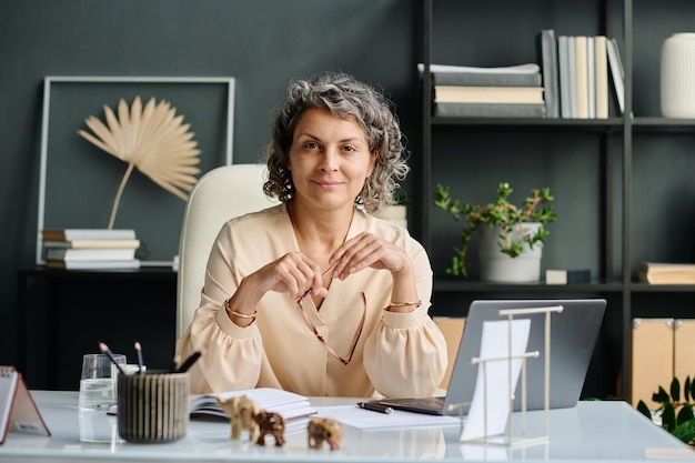 Femme directrice ou PDG souriante et mature, assise à son bureau devant un ordinateur portable