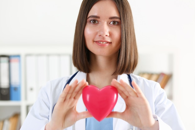 Femme docteur en médecine tenir dans les mains coeur jouet rouge devant sa poitrine