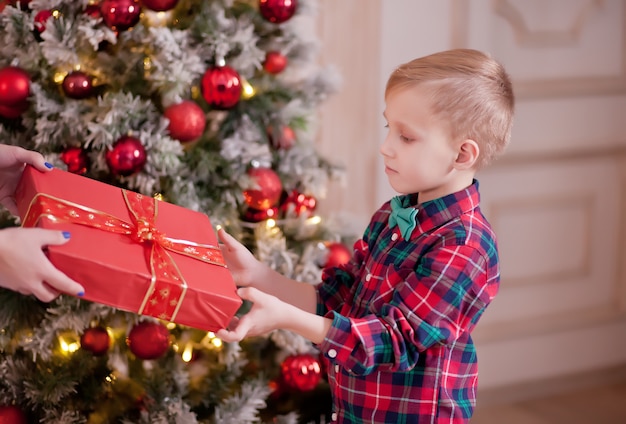 Femme donne un garçon mignon en chemise à carreaux coffret cadeau de Noël rouge avec arbre de Noël