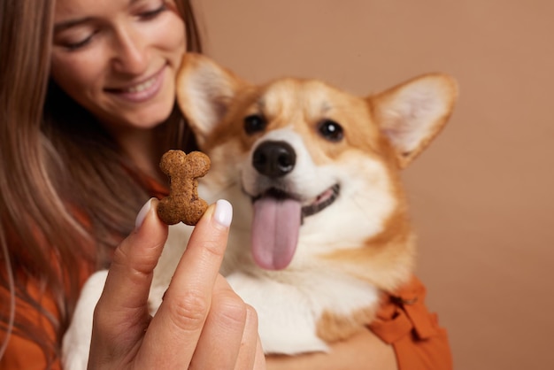 Photo une femme donne à son chien de la nourriture délicieuse en forme d'os sur un fond beige vide.