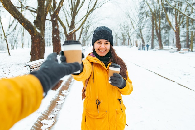 Une femme donne une tasse de café à un ami. réunion dans le concept de parc d'hiver enneigé