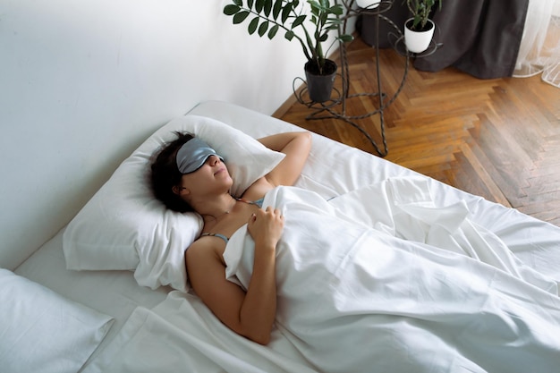 Femme dormant dans un masque de sommeil au lit avec des draps blancs