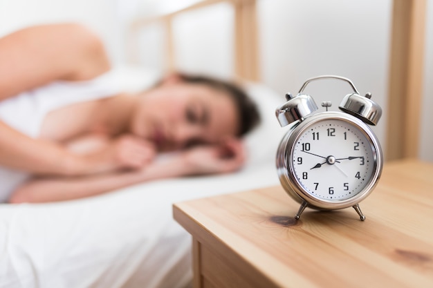 Femme Dormant Sur Un Lit Près Du Réveil Sur Un Bureau En Bois