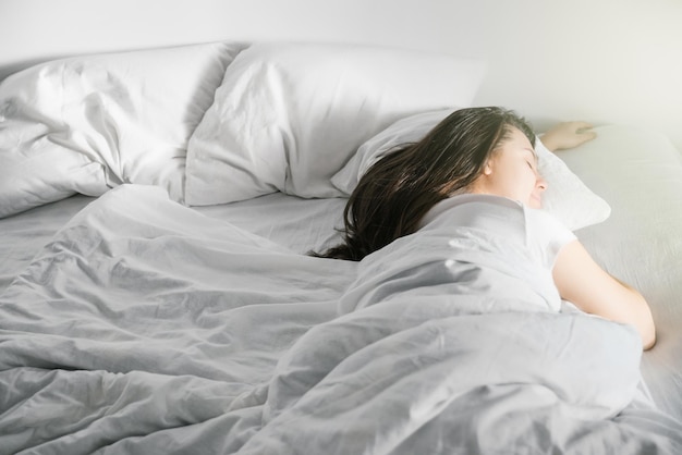 La femme dort dans le lit le soleil a pensé à la fenêtre