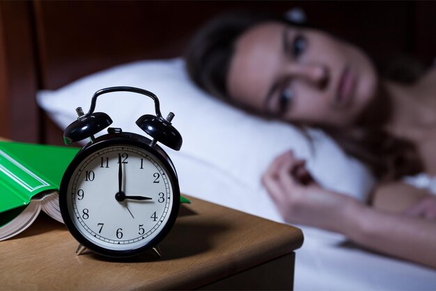 Une femme dort dans son lit avec une horloge qui indique " 5 ".