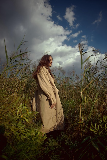 Femme douce rêveuse dans un imperméable beige dans la nature Jeune femme romantique dans les hautes herbes épaisses dans le champ Beauté naturelle jouissance de la vie