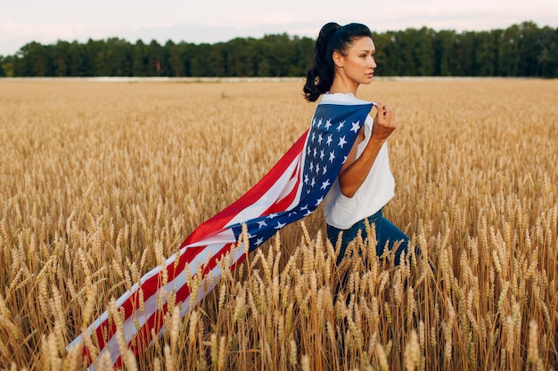 Femme avec drapeau américain dans le champ de blé au coucher du soleil. 4 juillet. Fête patriotique du jour de l'indépendance.