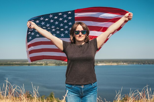 Une femme avec le drapeau de l'Amérique dans ses mains sur le fond de la baie aime la nature