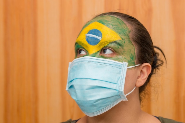 Femme avec le drapeau du Brésil peint sur son visage avec un masque d'hôpital bleu