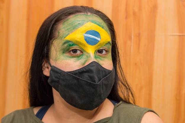 Femme avec le drapeau du Brésil peint sur son visage avec un masque noir