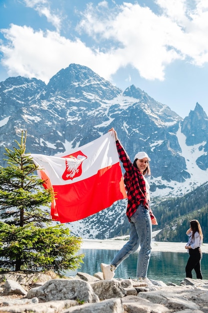 Une femme avec le drapeau de la Pologne se tient sur le rivage d'un lac Morskie Oko