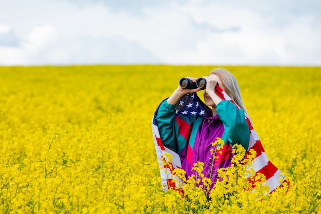 Femme avec drapeau USA et jumelles dans le champ de colza jaune